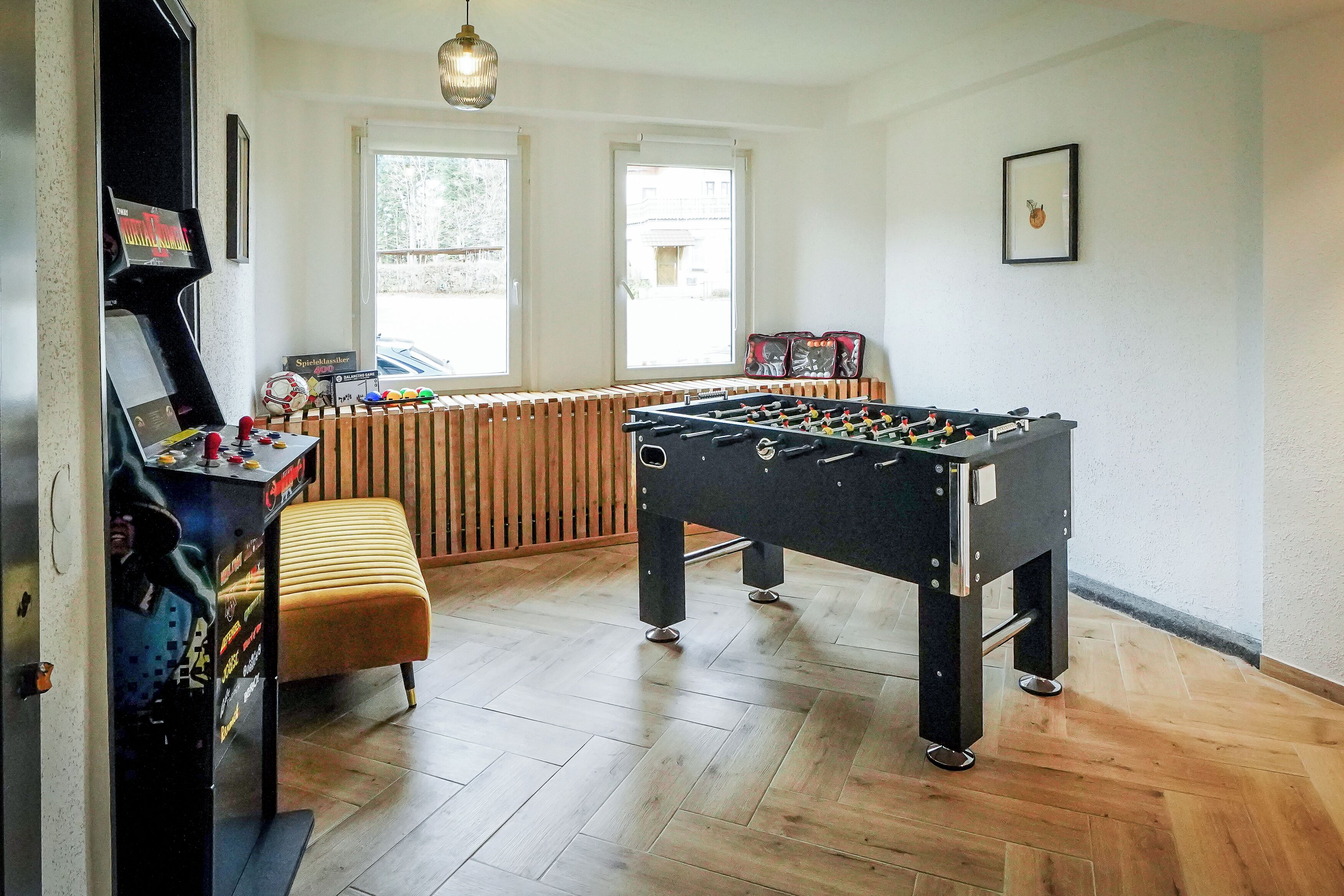 A room with a foosball table, a foosball table with a ball and figure, and a bench.
