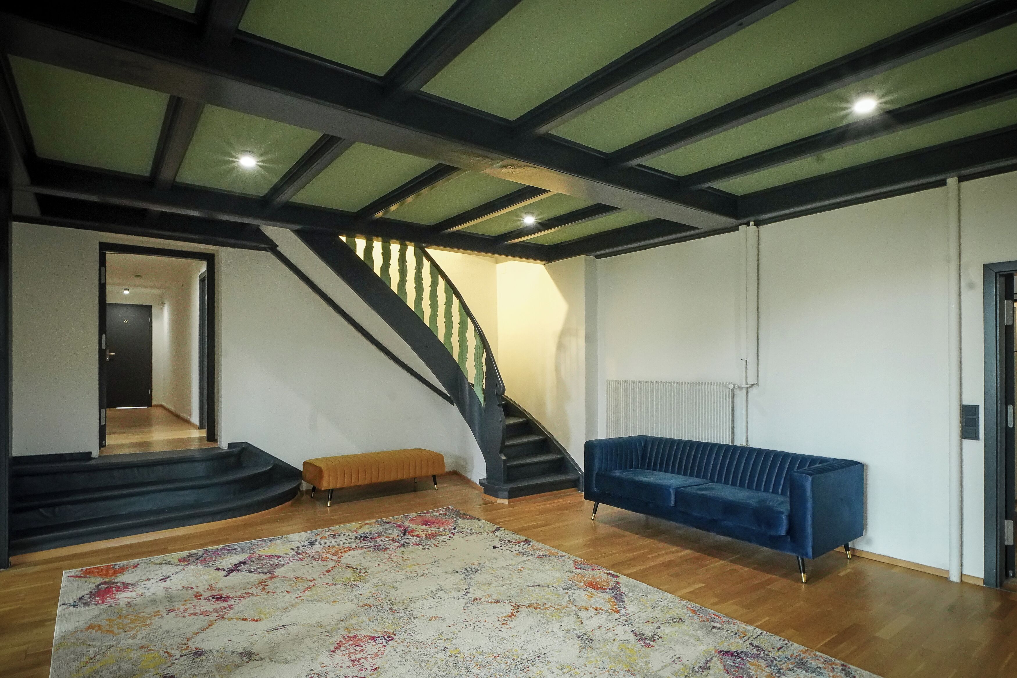 Ein geräumiges Wohnzimmer mit Treppe, einem blauen Sofa und einem farbenfrohen Teppich.