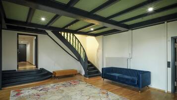 Ein geräumiges Wohnzimmer mit Treppe, einem blauen Sofa und einem farbenfrohen Teppich.