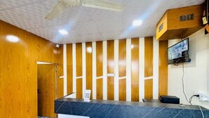 Ein Empfangsbereich mit einer Wandpaneele aus Holz, einer Theke aus schwarzem Marmor, einem Deckenventilator und einem montierten Fernseher.