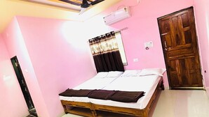 Ein Schlafzimmer mit einem Bett, einem Deckenventilator, einer Klimaanlage, einer Holztür und einem kleinen Tisch.
