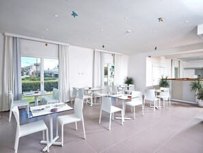 A modern dining area with white furniture and large windows offering a view of the cityscape. - Hotel with panoramic swimming pool in porto San Paolo (Porto San Paolo)