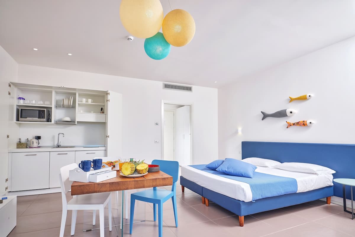 Una habitación de hotel moderna con cama, una mesa de comedor con sillas, una zona de cocina y peces decorativos en la pared.