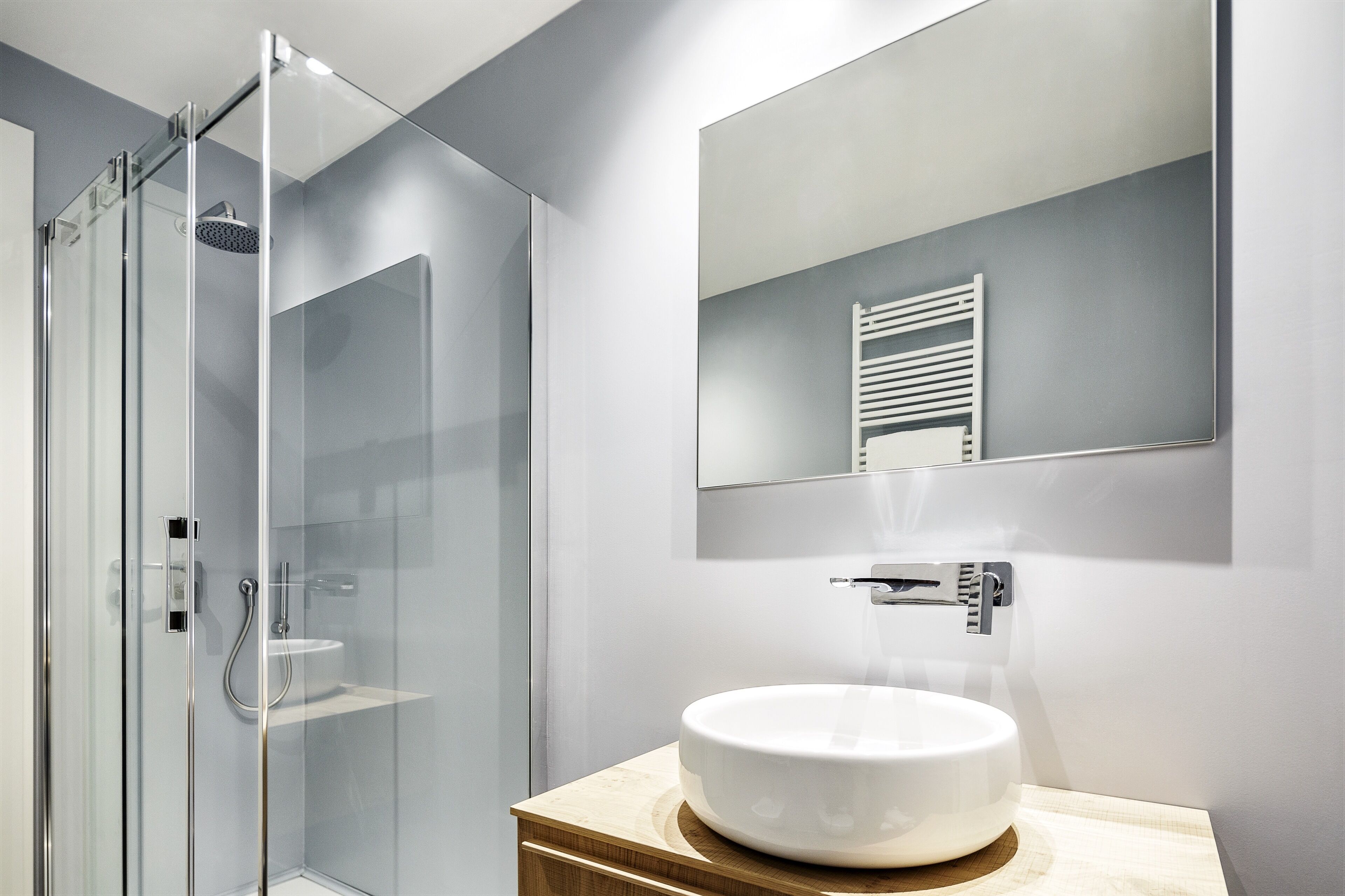 Un bagno moderno con cabina doccia in vetro, un lavandino bianco e uno specchio sopra il lavandino.
