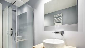Un bagno moderno con cabina doccia in vetro, un lavandino bianco e uno specchio sopra il lavandino.