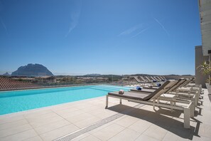 A poolside area with lounge chairs, a clear blue pool, and a mountainous backdrop. - Hotel with panoramic swimming pool in porto San Paolo (Porto San Paolo)