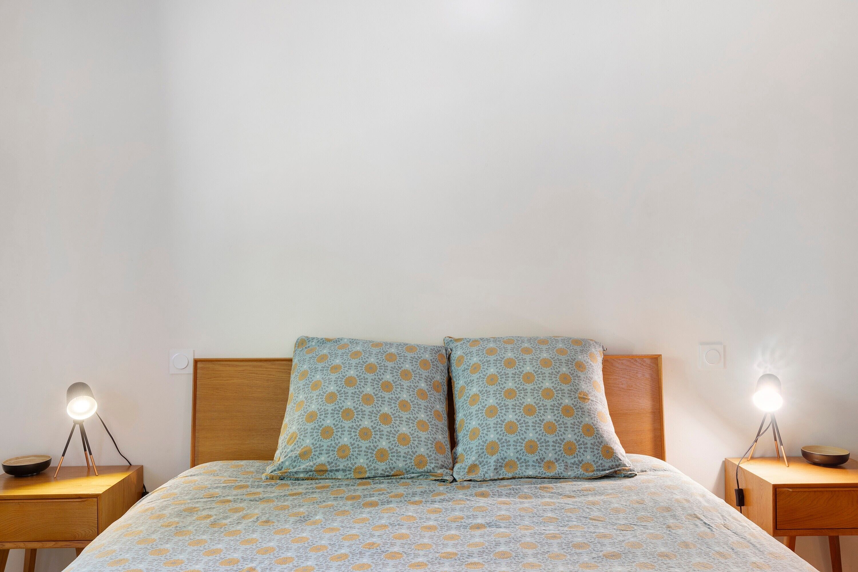 Una cama con colcha estampada, dos mesitas de noche con lámparas y un cabecero de madera.