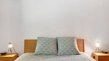 A bed with a patterned bedspread, two bedside tables with lamps, and a wooden headboard.