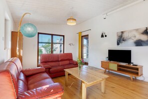 Ett vardagsrum med en röd lädersoffa, ett träbord, en tv på ett träställ och ett stort fönster med persienner.
