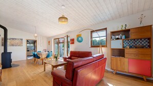 Amplia sala de estar con un sofá de cuero rojo, una mesa de comedor de madera y una cocina visible a través de una puerta abierta.