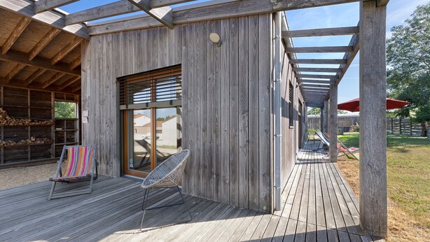 Una terraza de madera con un área de estar cubierta, una silla y una mesa.