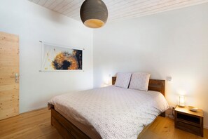 Ett sovrum med en säng i trä, ett nattduksbord med en lampa, en abstrakt tavla som hänger på väggen och en dörr i trä.