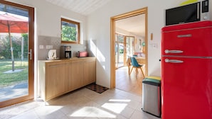 Una cocina con un refrigerador rojo, armarios de madera, un ventanal y una puerta que da a un comedor.