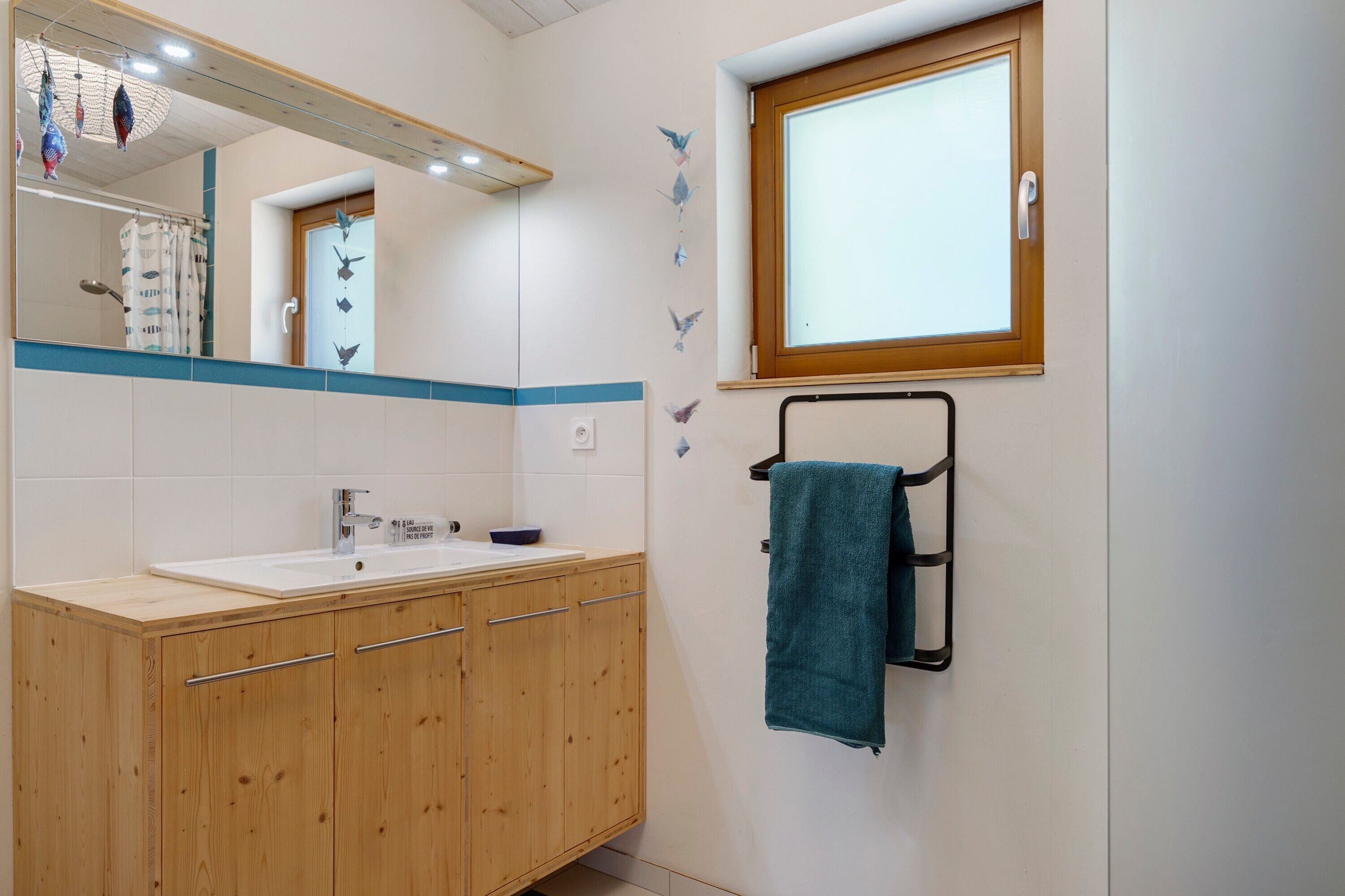 Une salle de bain avec un meuble-lavabo en bois, un miroir, une fenêtre et un porte-serviettes.