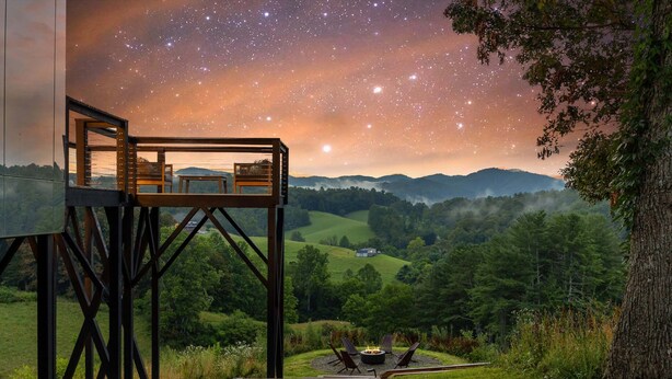 A wooden deck with a fire pit and seating, overlooking a lush valley and a starry night sky. - Elevated Invisible Cabin, Hot Tub, Views (Marshall)