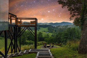 A wooden deck with a fire pit and seating, overlooking a lush valley and a starry night sky. - Elevated Invisible Cabin, Hot Tub, Views (Marshall)