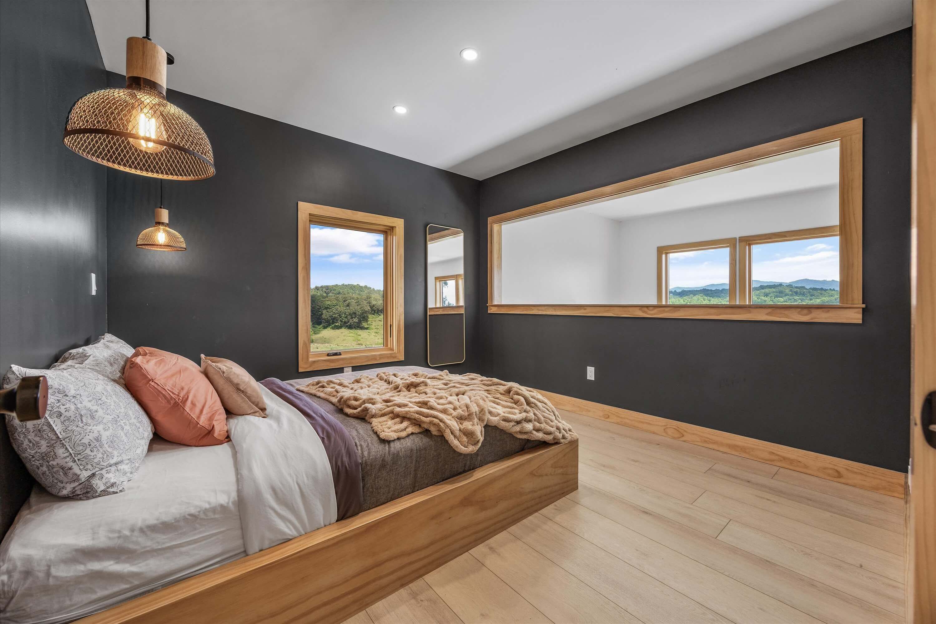 Camera da letto moderna con un letto grande, una testiera in legno, uno specchio ampio e vista sull'esterno.