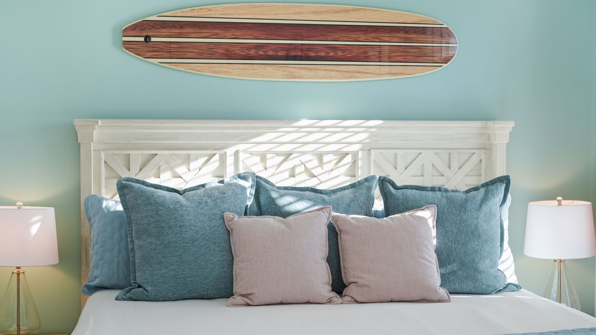 Un dormitorio con cama, almohadas y una tabla de surf colgada en la pared.