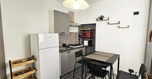 Eine kompakte Küche mit Kühlschrank, Mikrowelle und Spüle. Ein kleiner Esstisch mit Stühlen ist vorhanden.