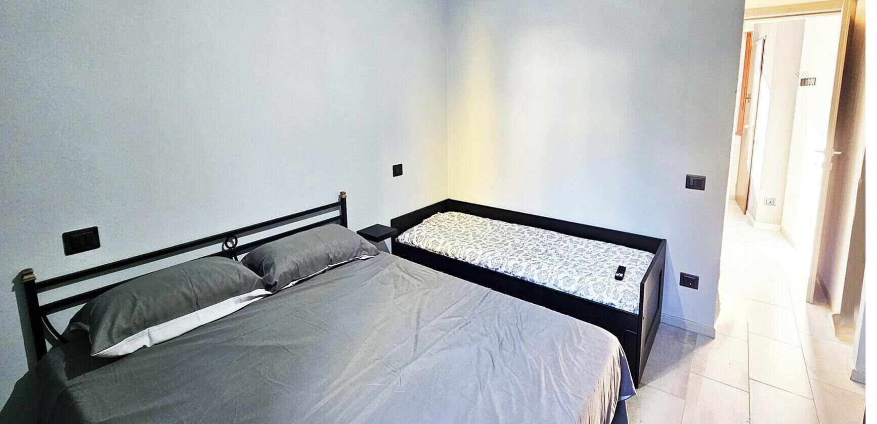 A bedroom with two beds, a door, and a light switch on the wall.