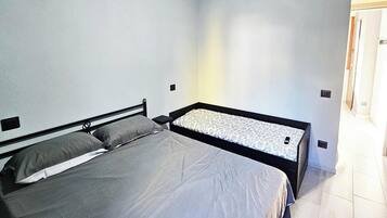 A bedroom with two beds, a door, and a light switch on the wall.