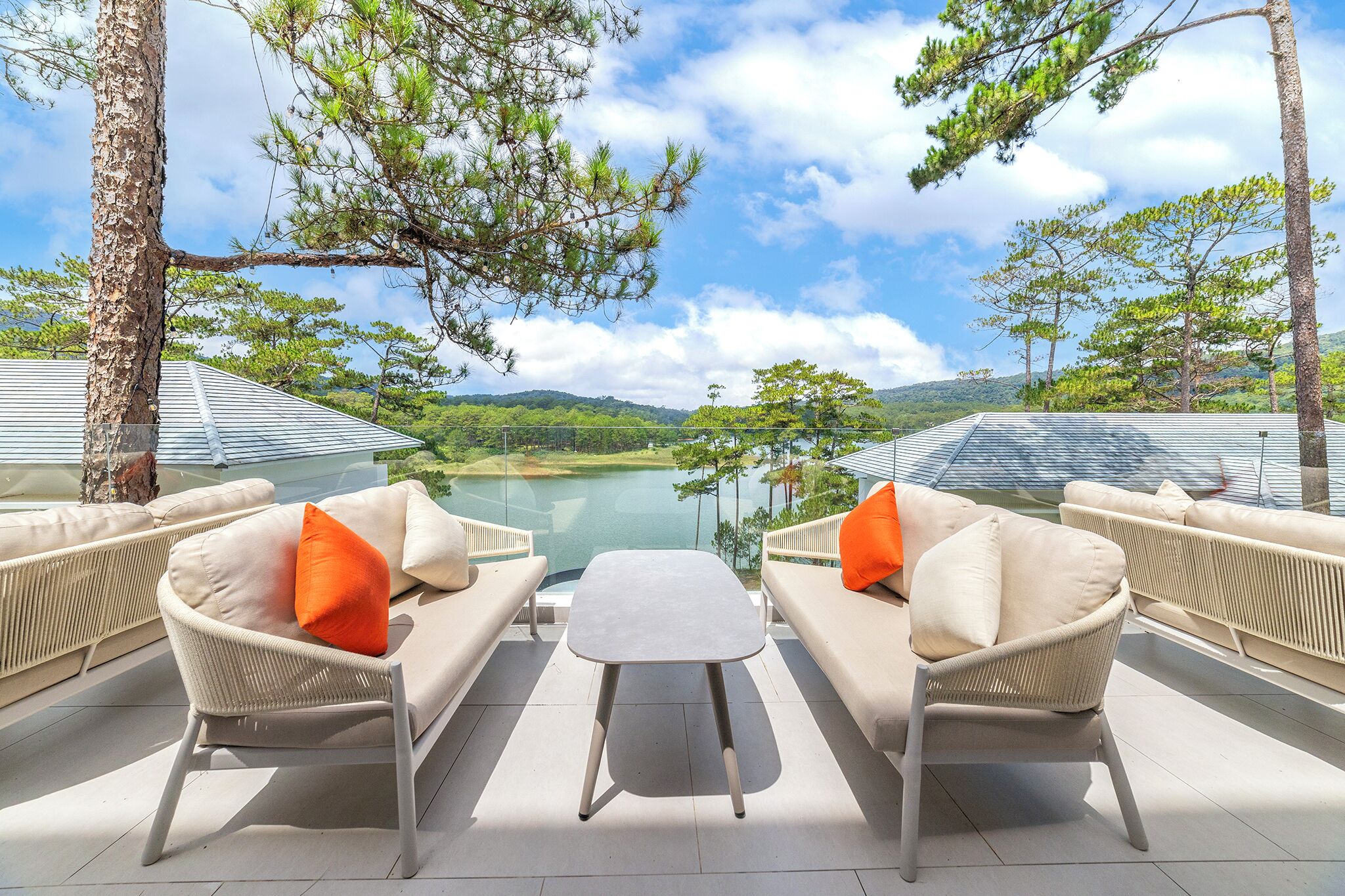 A terrace with wicker furniture, a small table, and a view of a lake and hills.