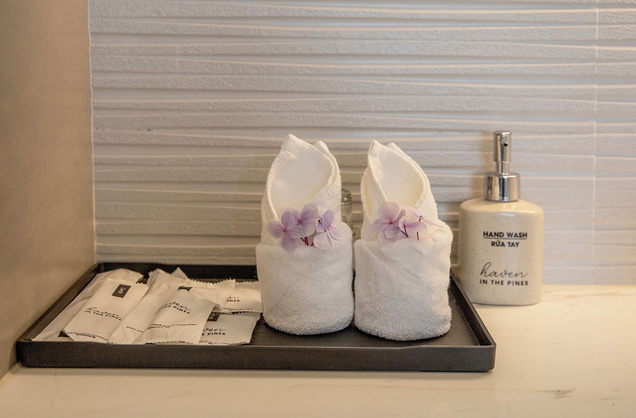 A tray with towels, a hand wash dispenser, and toiletries on a hotel counter.