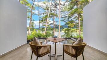 Ein Balkon mit zwei Korbstühlen und einem kleinen Tisch, mit Blick auf eine üppige Landschaft mit Bäumen und einem Gewässer.