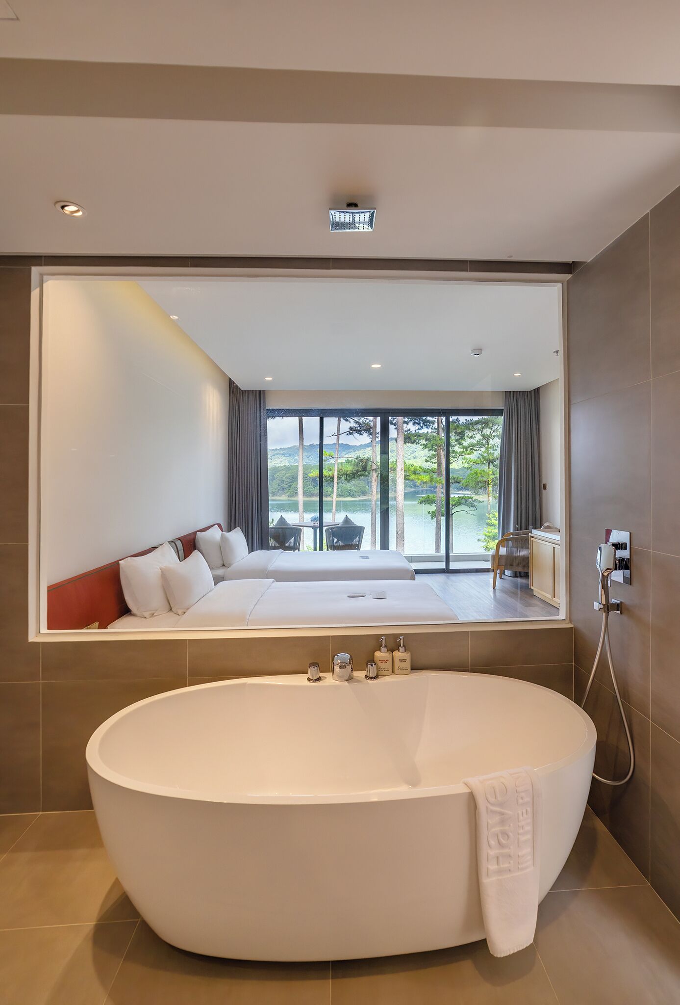A modern hotel room with a large bathtub, a bed with white linens, a view of a lake, and a large window.