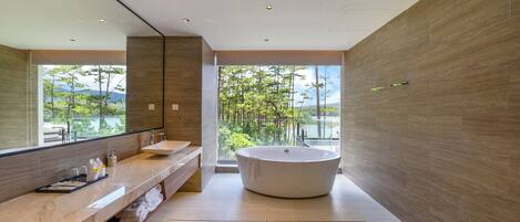 Une salle de bain moderne avec une grande baignoire, un meuble-lavabo avec un miroir et une vue sur les arbres et l’eau.