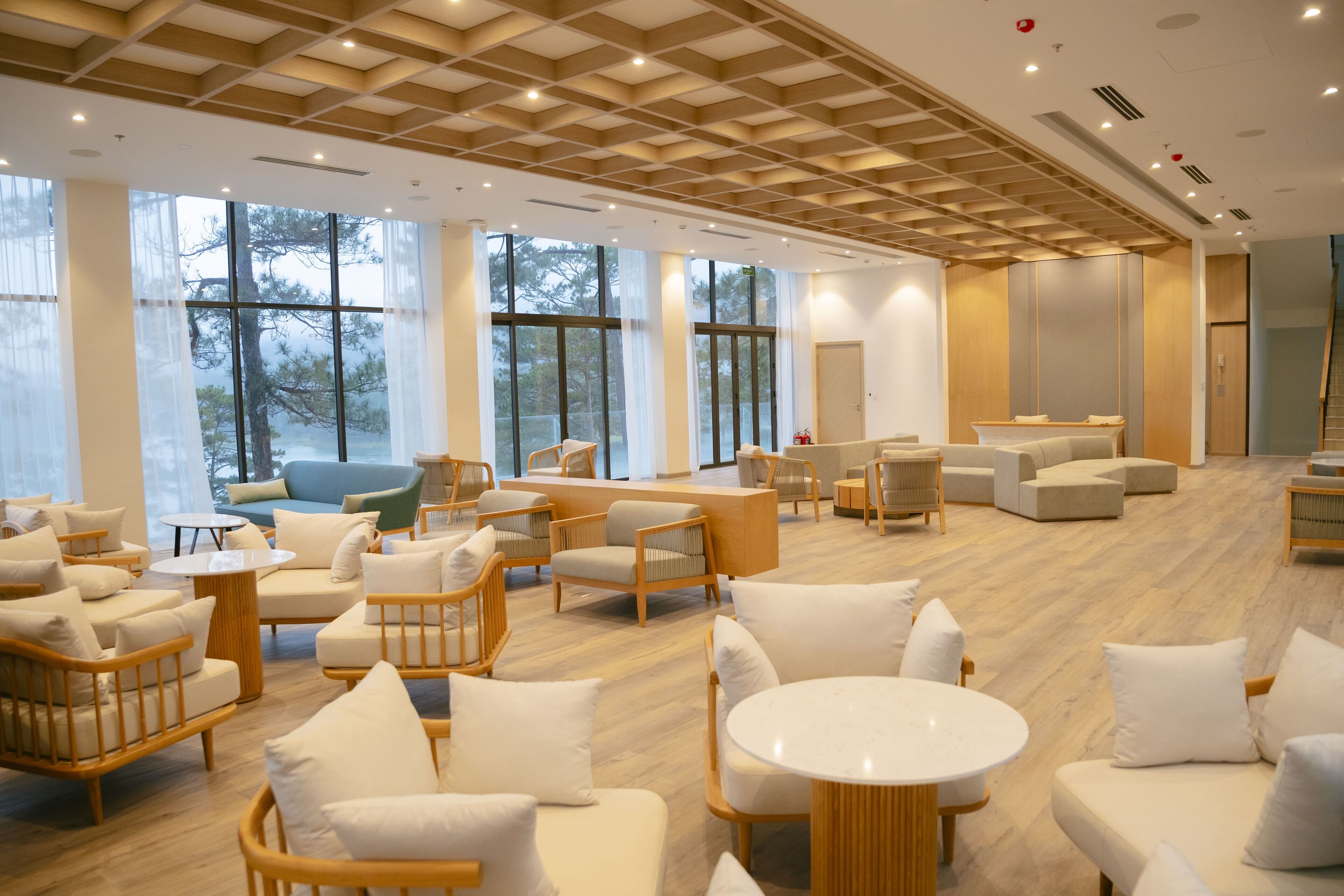 A spacious lobby with modern furniture, large windows, and a wooden ceiling.