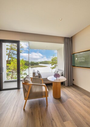 Una habitación moderna con un gran ventanal, un sofá, una mesita y una pantalla que muestra 'HAVEN IN THE PINES'.