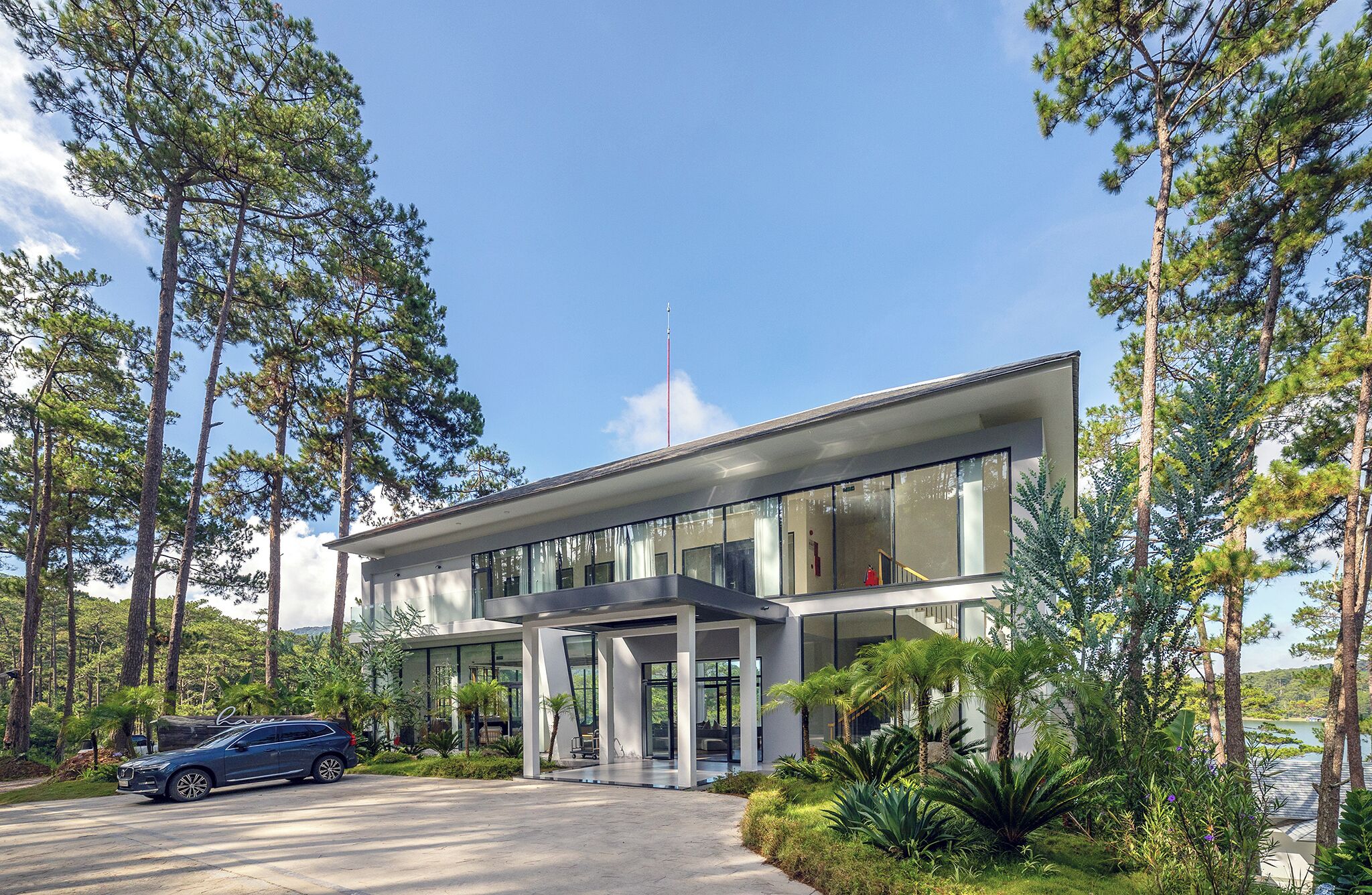 Een modern gebouw met een glazen gevel, omgeven door hoge bomen en een heldere lucht.