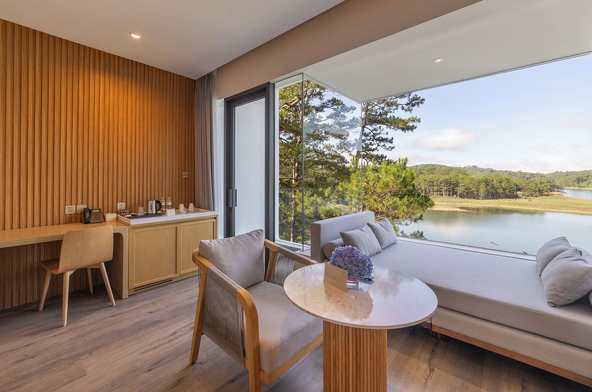 A modern room with a wooden wall, a dining area, a sofa with cushions, and a view of a lake.