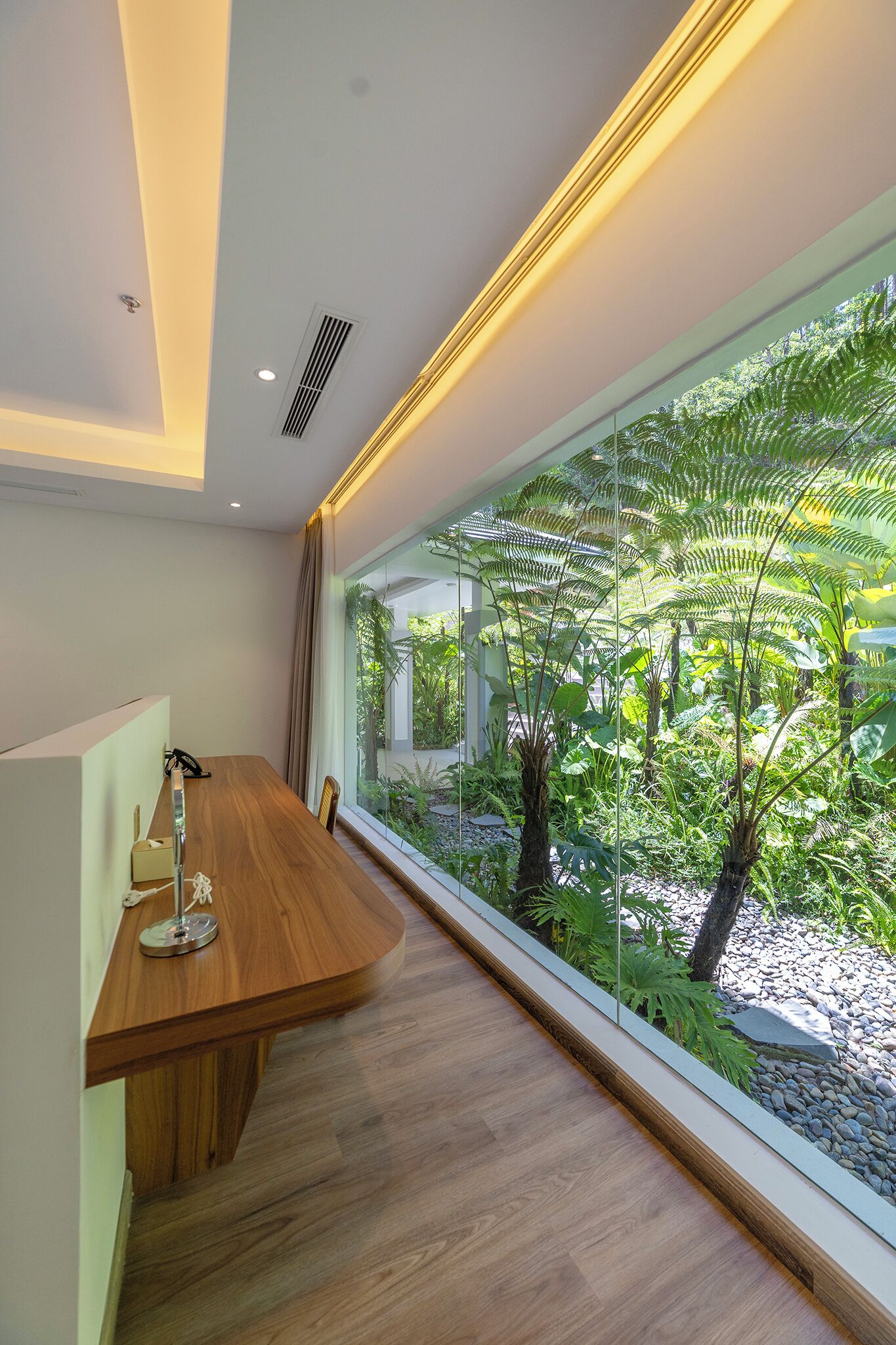 A modern room with a wooden desk, a lamp, and a large window overlooking a garden.
