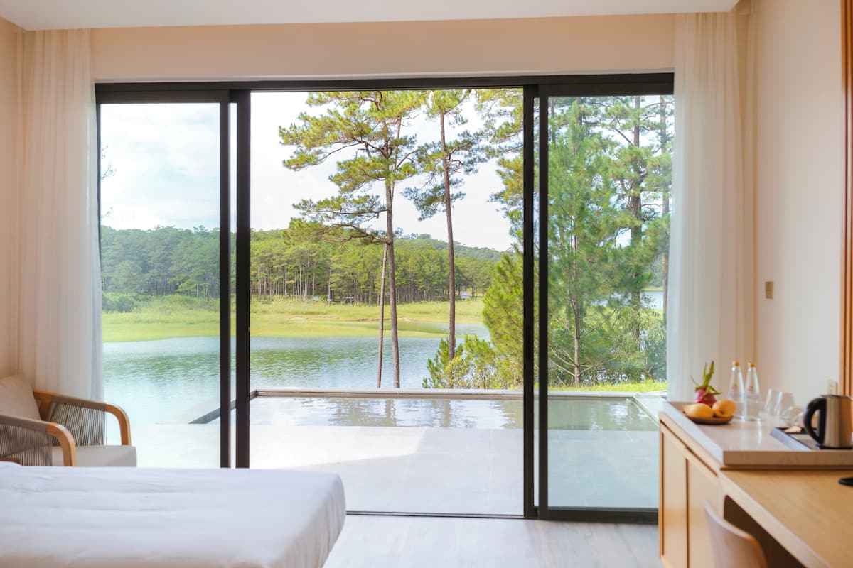 A bedroom with a large sliding glass door leading to a balcony with a view of a lake and trees.