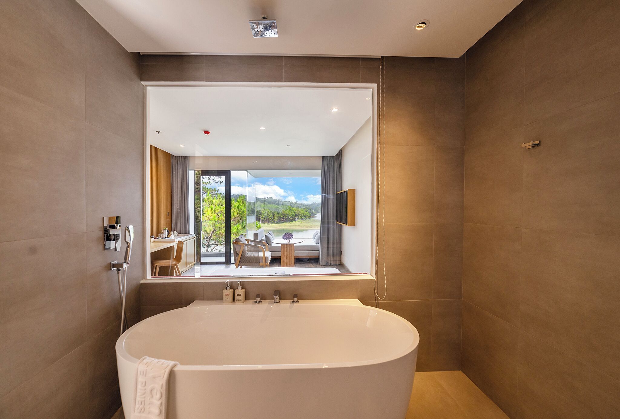 A modern bathroom with a large bathtub, a shower area, and a view of an outdoor seating area through a large window.