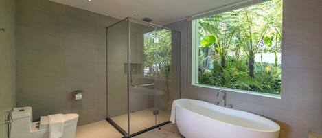 A modern bathroom with a glass-enclosed shower, a freestanding bathtub, and a window providing a view of greenery.