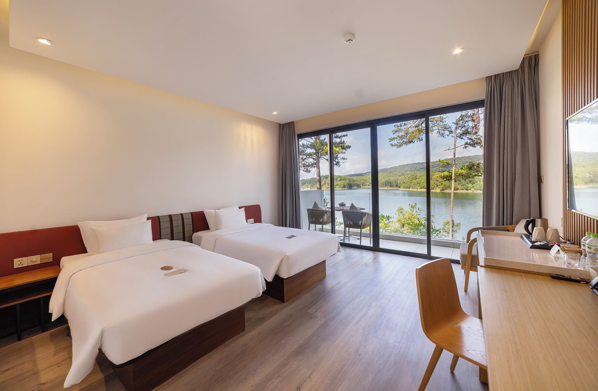 Een hotelkamer met twee bedden, een bureau en uitzicht op een meer.
