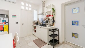 Eine kleine Küche mit weißen Schränken, einer Mikrowelle, einer Kaffeemaschine und einem kleinen schwarzen Regal.