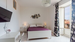 Ein Schlafzimmer mit Bett, Nachttischen, einem an der Wand befestigten Fernseher, einer Wanddekoration und einem Fenster mit Vorhängen.