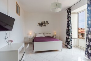 A bedroom with a bed, bedside tables, a TV mounted on the wall, a decorative wall piece, and a window with curtains. - Alex Baroque near Beach & Etna by Wonderful Italy (Catania)