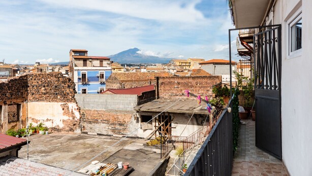 Eine Dachterrasse mit Bergblick, eine Mischung aus alten und neuen Gebäuden sowie ein Balkon mit Blumentöpfen.
