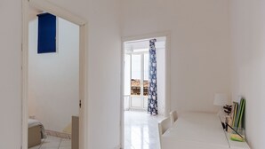 Ein Zimmer mit weißem Schreibtisch, einem Stuhl und einem Bett mit blauer Vorhang.