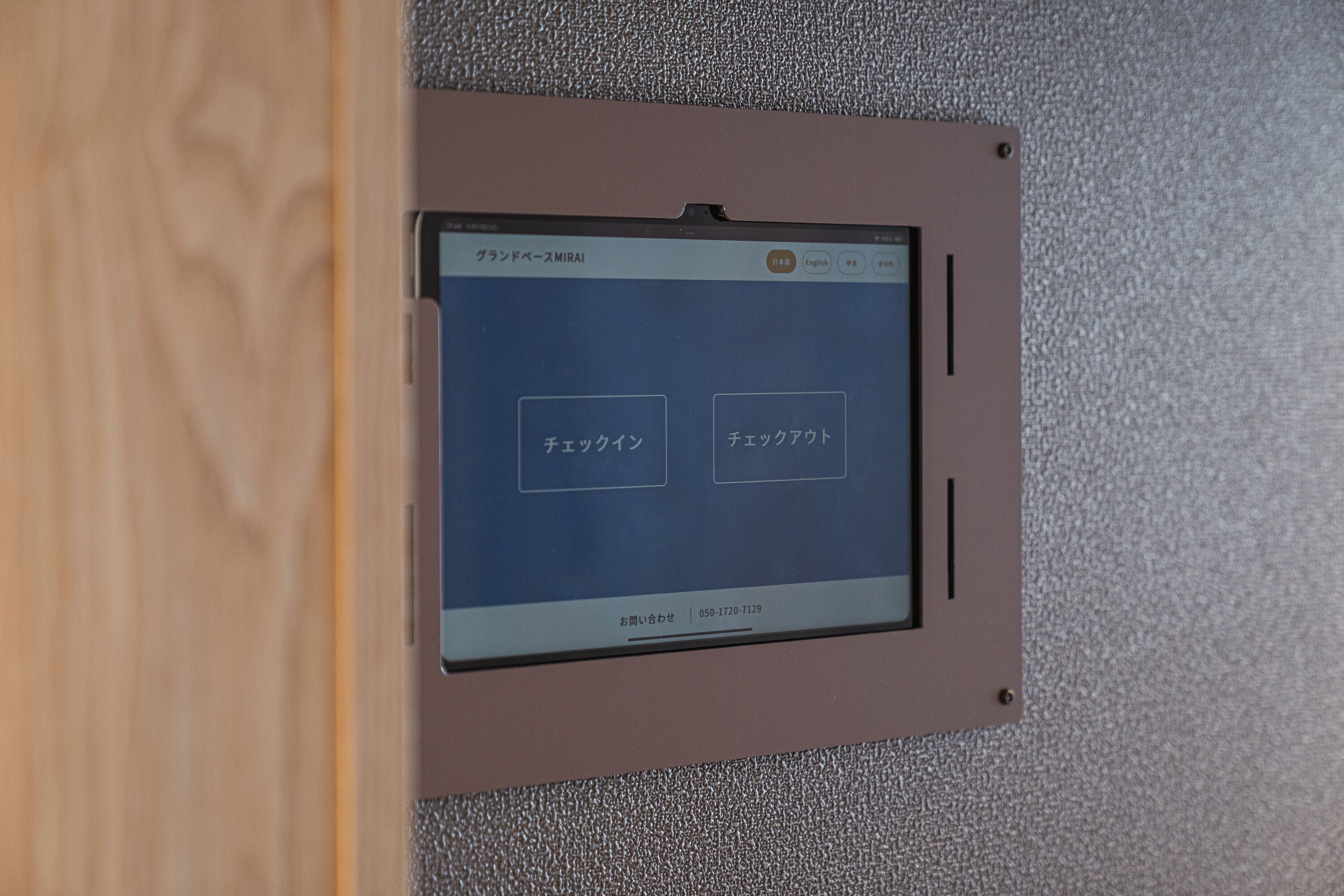 A digital display with Japanese text, mounted on a textured wall.
