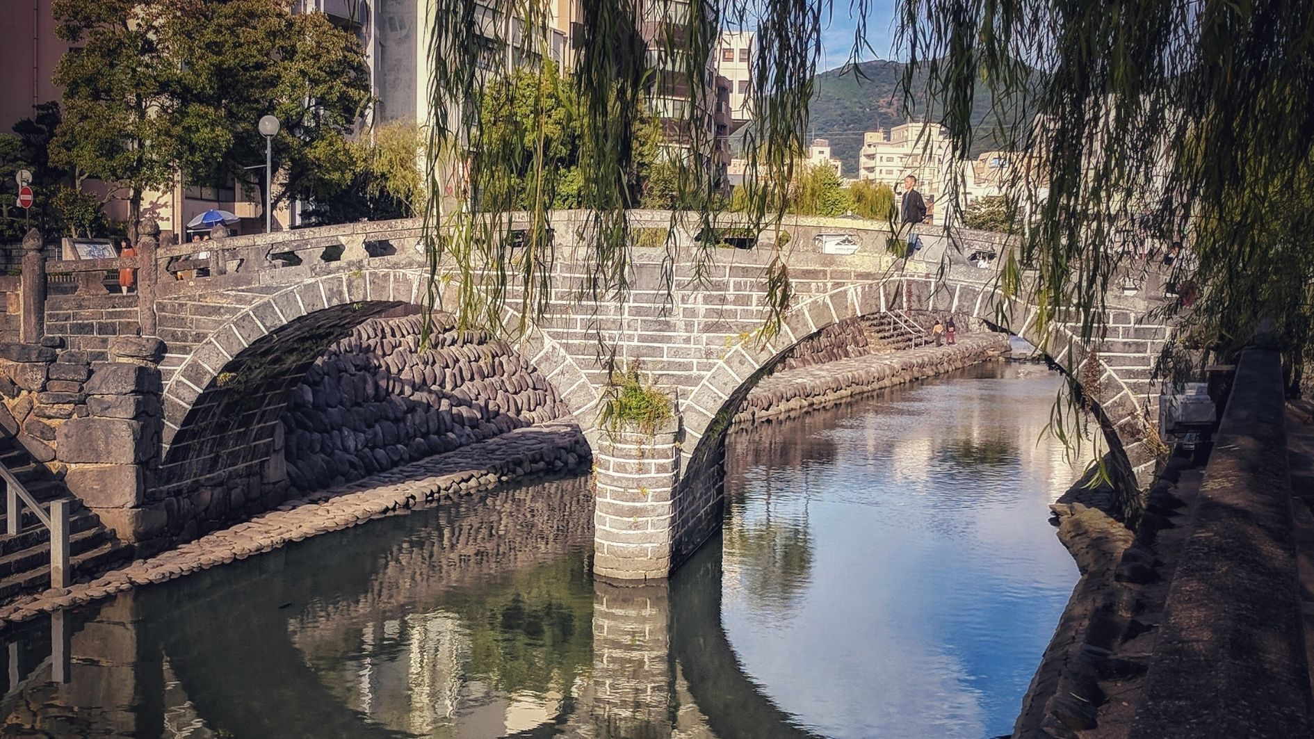 Een stenen brug over een kalme rivier, met een helder uitzicht op gebouwen in de verte.
