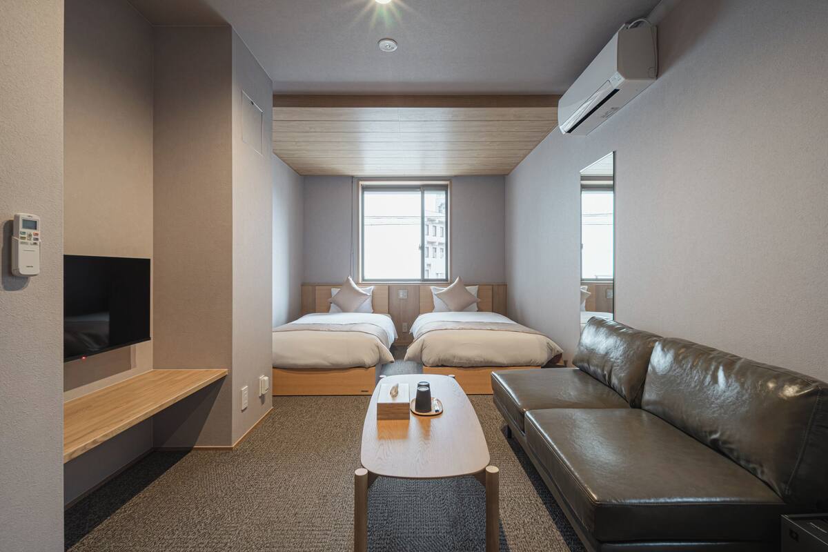 A compact hotel room with two beds, a sofa, a TV, and a small table.