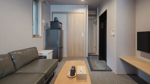 A compact living space with a sofa, a coffee table, a refrigerator, a television, and a shower area. - GRAND BASE MIRAI (Nagasaki)