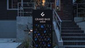 A sign for Grand Base Mirage with a geometric design and a staircase leading up. - GRAND BASE MIRAI (Nagasaki)