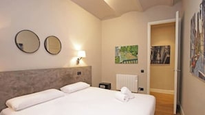 A hotel room with a large bed, two bedside tables, a wall-mounted mirror, a painting, and a radiator. - Spacious 2BR, quick access to Downtown (Barcelona)